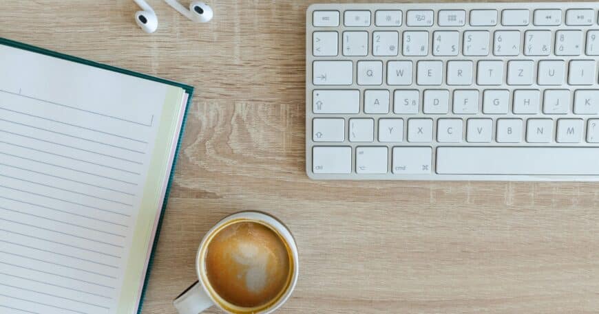 coffee latte near white wireless keyboard and Apple EarPods on the table photography